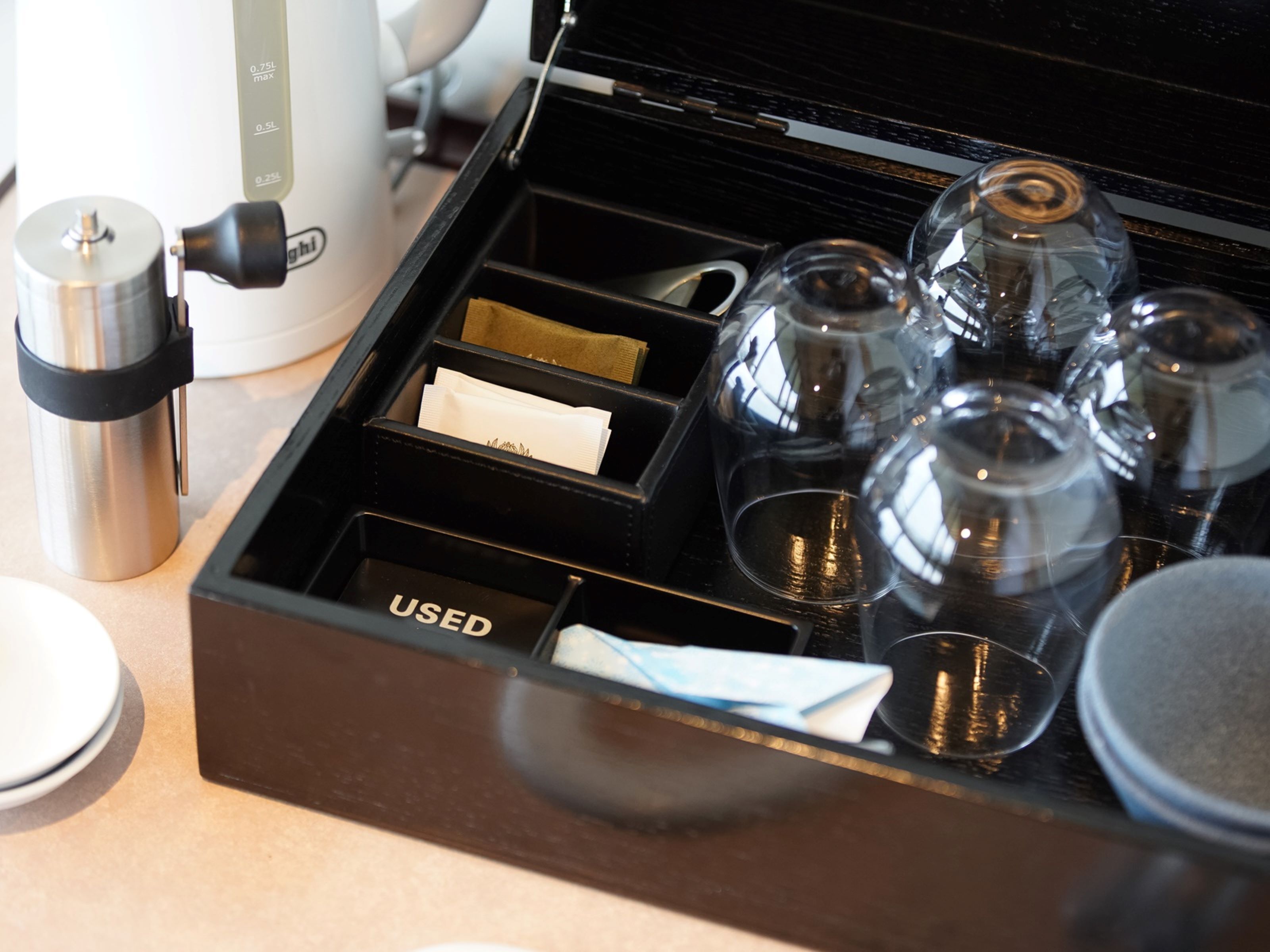 A drawer with compartments containing used napkins, a thermos, and glass tumblers.