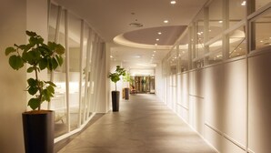 Un pasillo moderno de hotel con paredes de vidrio, plantas en macetas y suelo pulido.