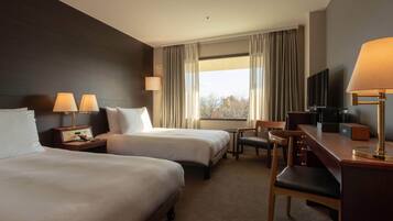 A hotel room with two beds, a desk with a chair, a television, and a window with curtains.