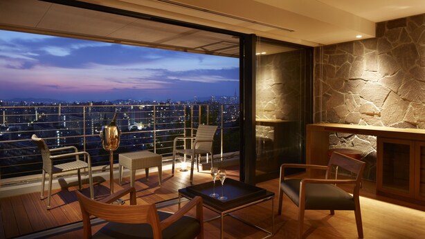 Un salón moderno con vistas panorámicas a la ciudad, que presenta una pared de acento de piedra, mobiliario de madera y una partición de vidrio.