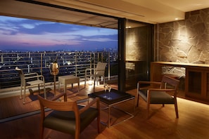 Un salón moderno con vistas panorámicas a la ciudad, que presenta una pared de acento de piedra, mobiliario de madera y una partición de vidrio.