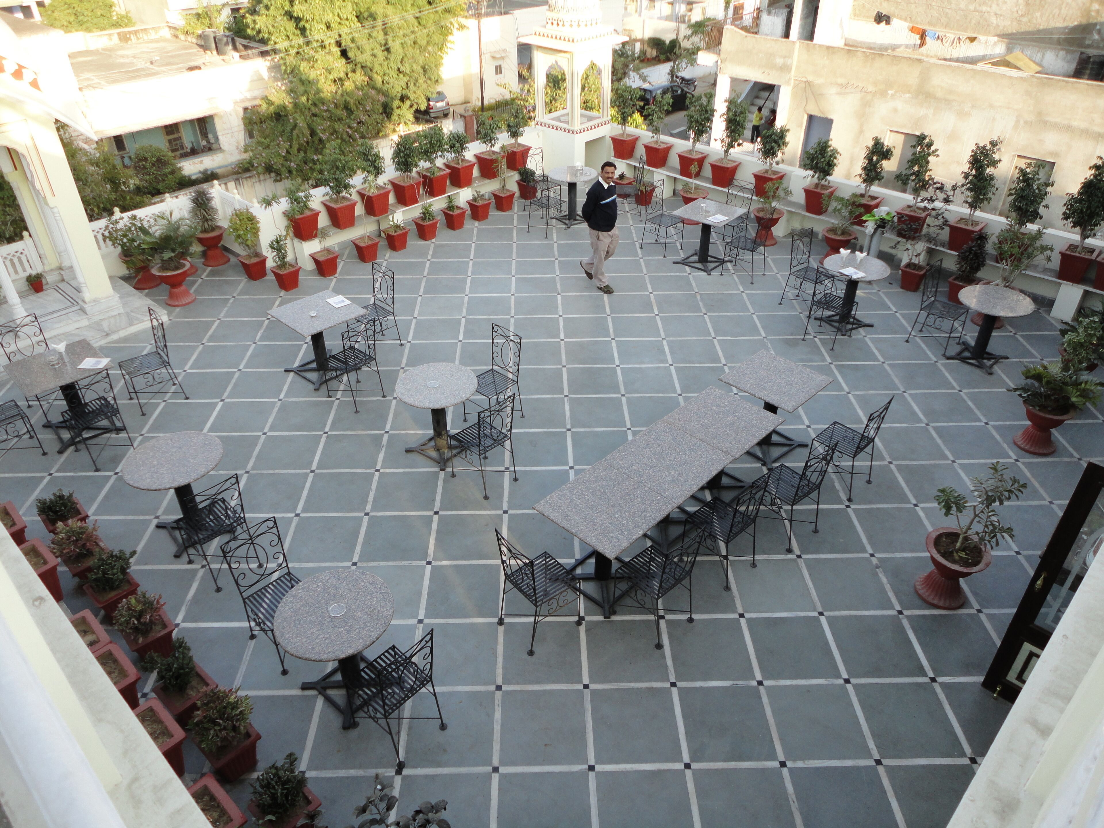 Un patio con mesas al aire libre, plantas en macetas y una fuente central.