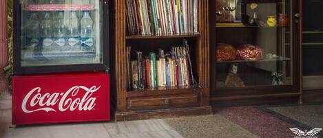 A Coca-Cola refrigerator, a bookshelf with various books, and a display case with cigarettes.