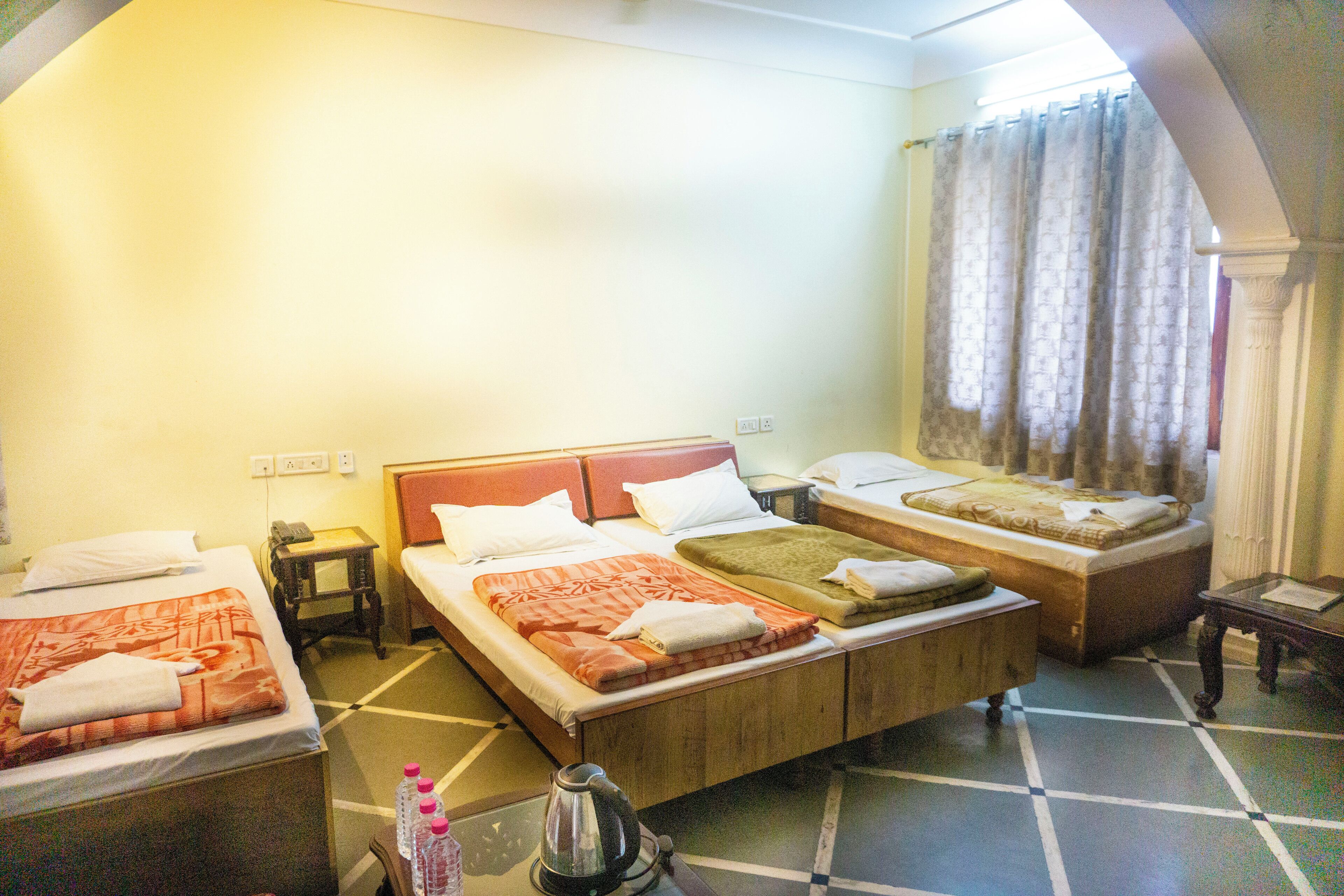 A hotel room with two single beds, a sofa bed, a small table, and a kettle.