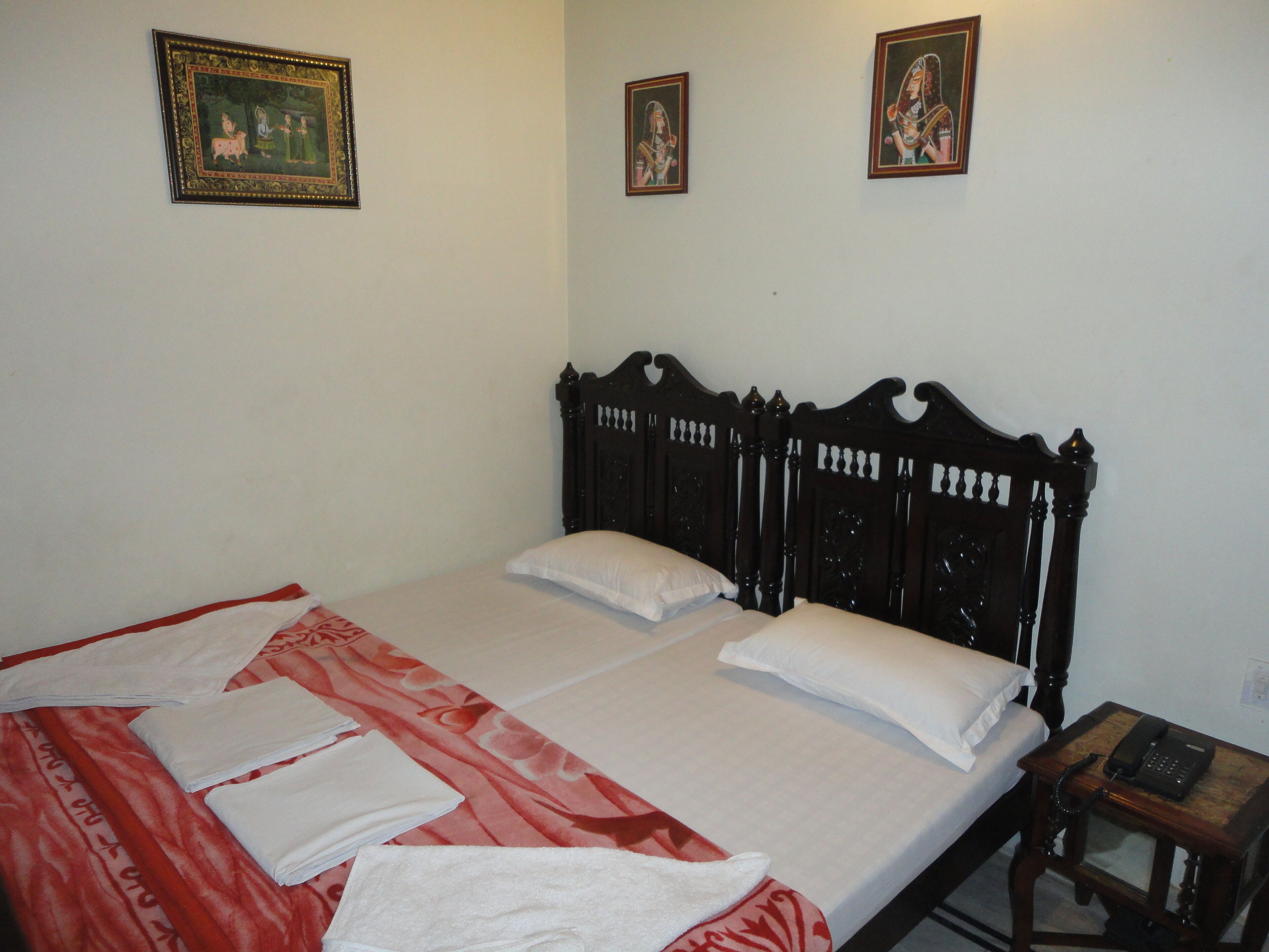 A neatly made bed with white linens, a red patterned bedspread, and a wooden headboard. There are two framed artworks on the wall above the bed.