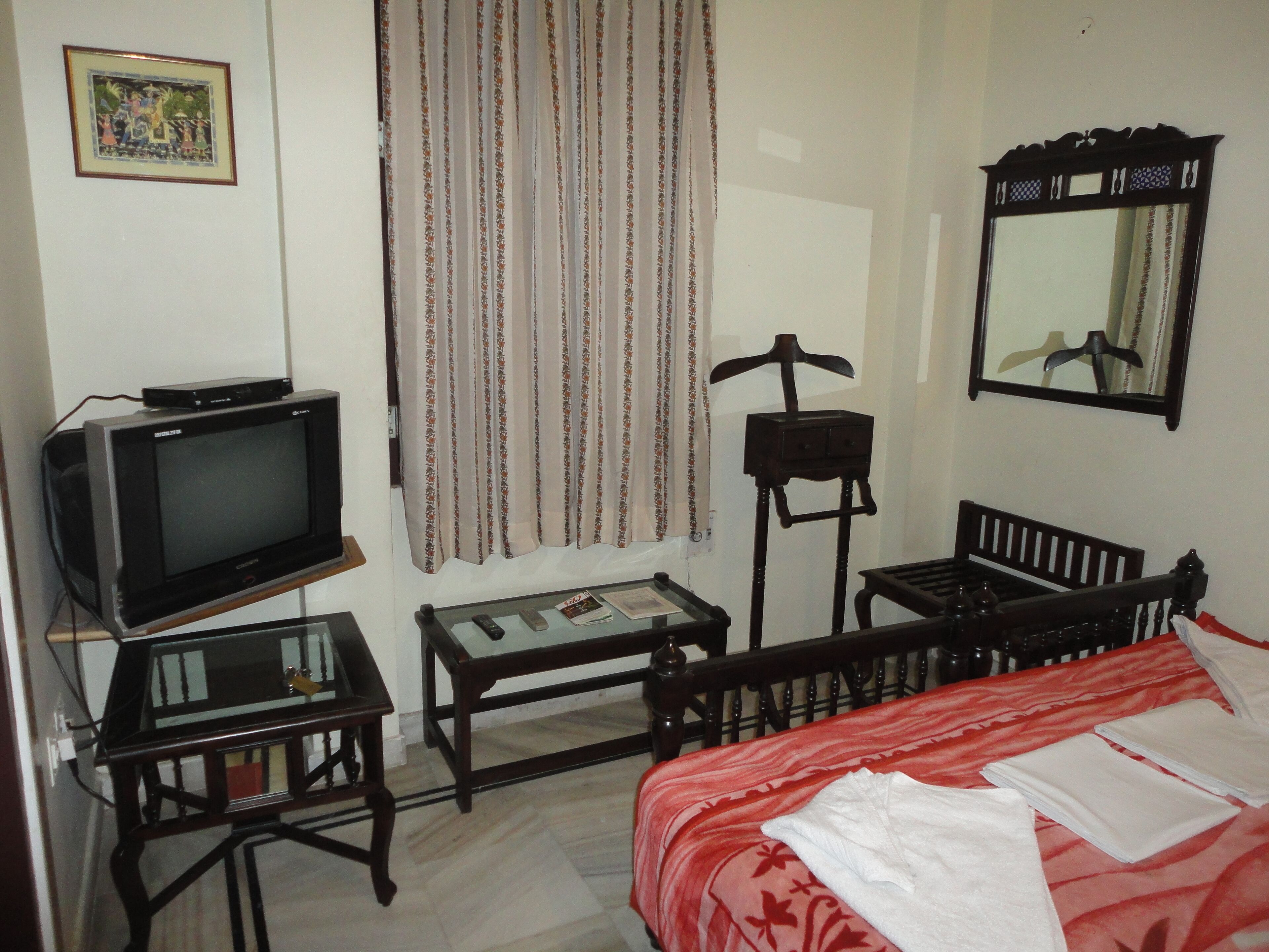 A small, simple room with a bed, a television, a small table, a chair, and a mirror.