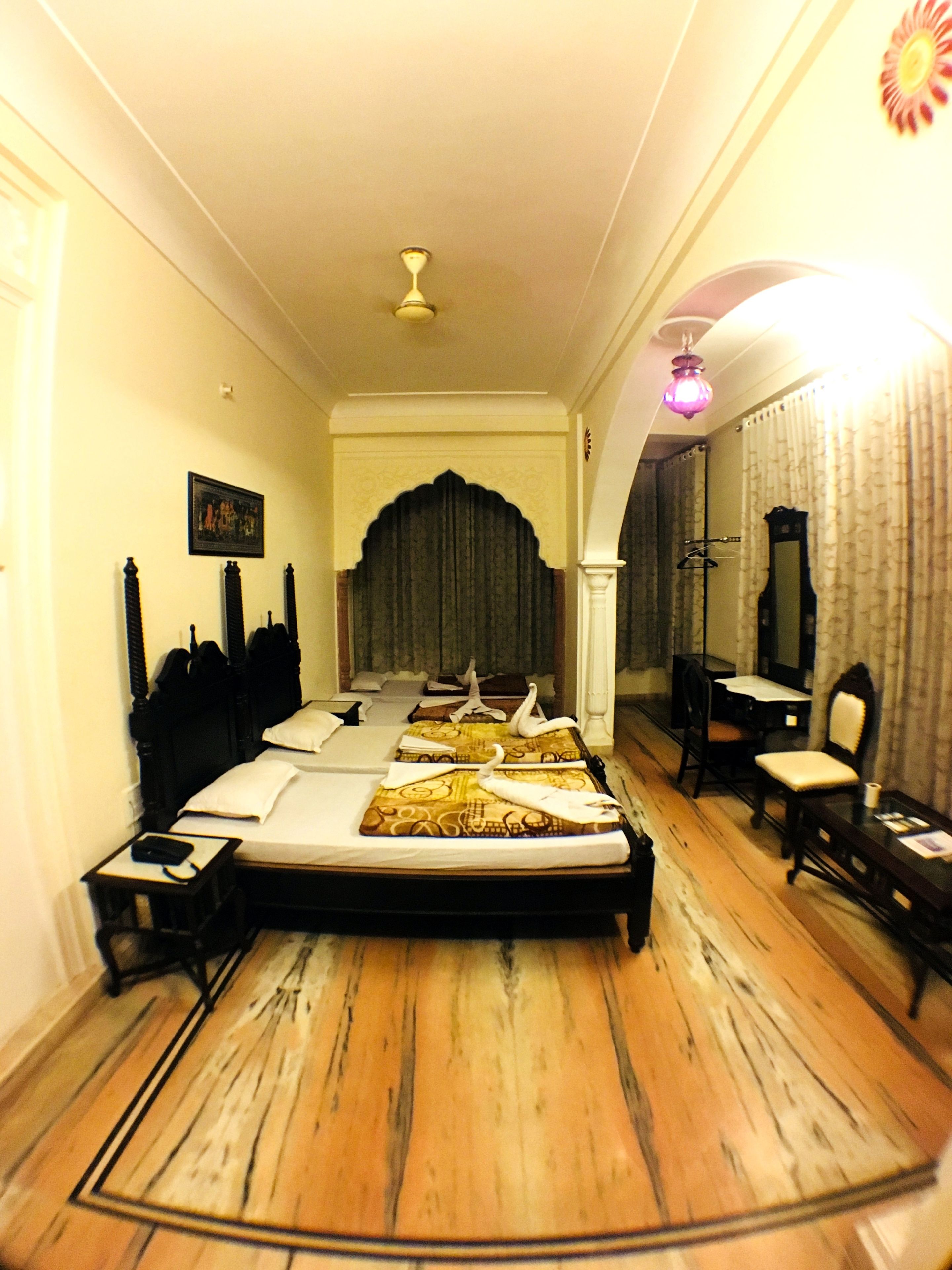 Une chambre d’hôtel avec un lit, un bureau, une chaise, un miroir et un ventilateur de plafond.