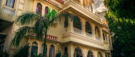 Traditional building with ornate balconies and arched windows, surrounded by lush greenery.