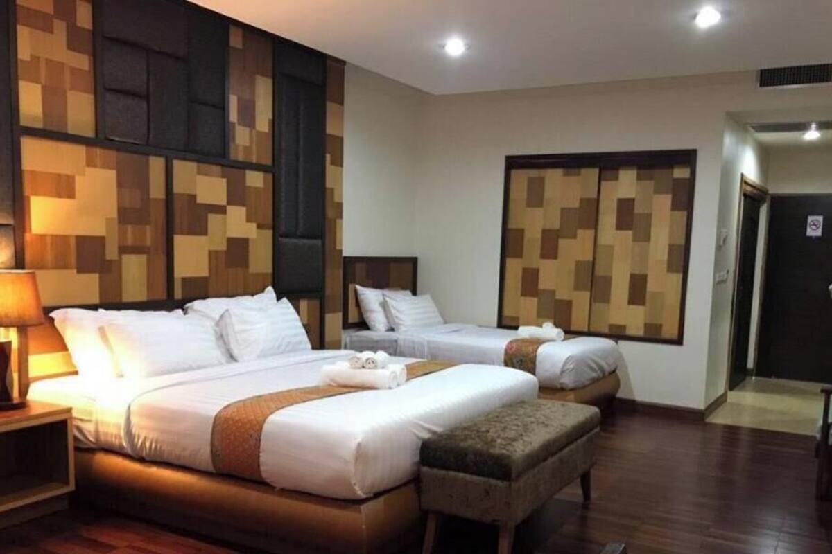 A hotel room with two beds, a nightstand, a lamp, a wooden floor, and a wall with a pixelated pattern.