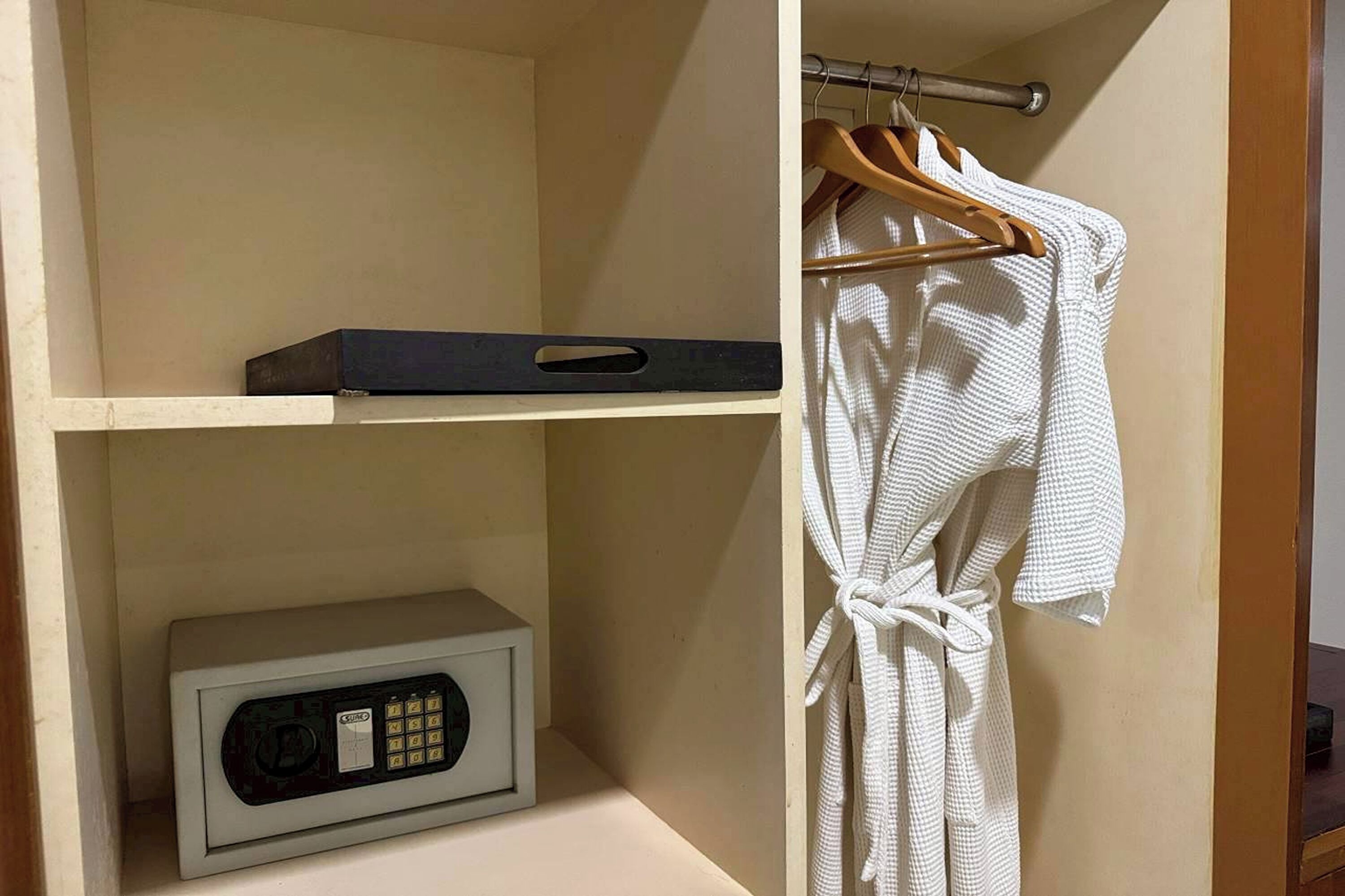 Une pièce dans laquelle on peut voir une robe blanche suspendue à un cintre en bois, un objet noir sur l’étagère supérieure et un appareil blanc sur l’étagère inférieure.