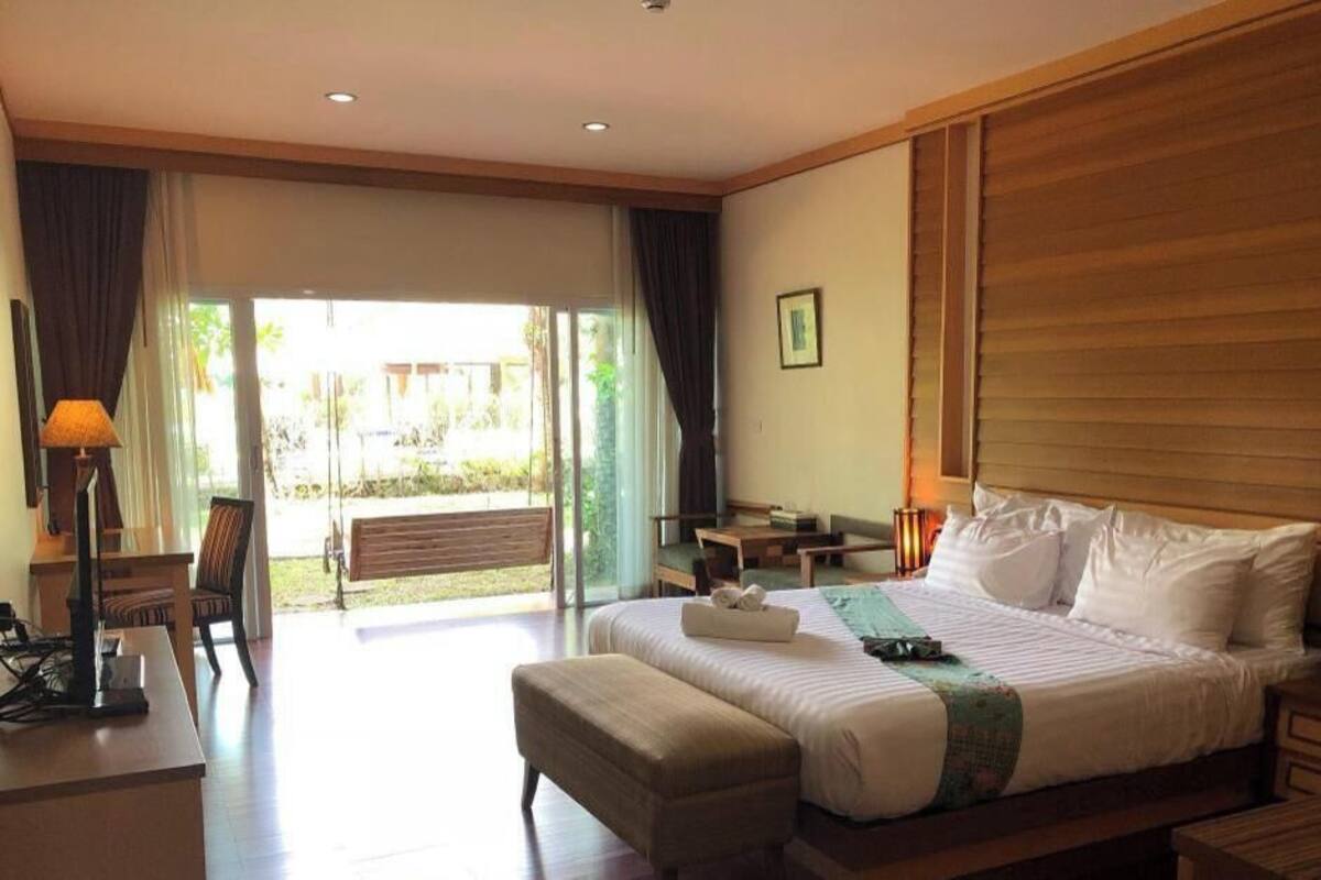 A hotel room with a large bed, a desk, a chair, a lamp, and a view of the outdoors.