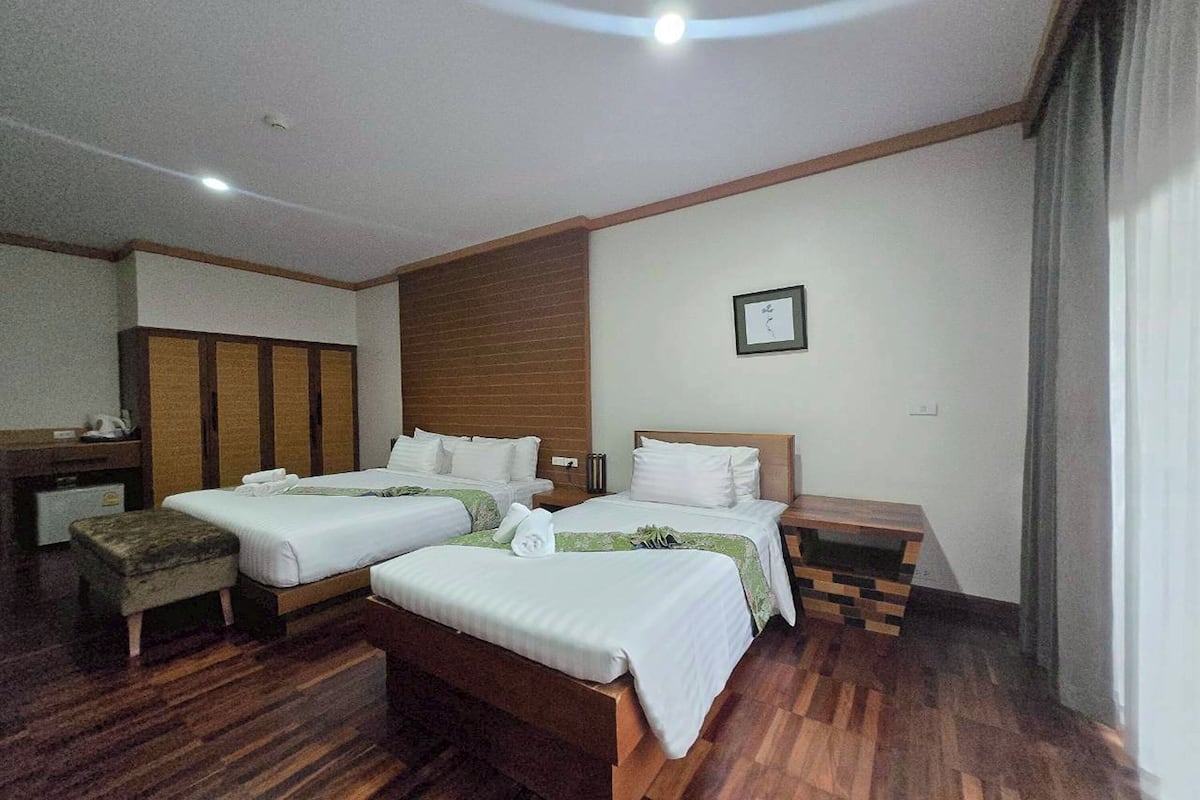 Habitación de hotel con dos camas, suelo de madera, un escritorio pequeño y una ventana con cortinas.