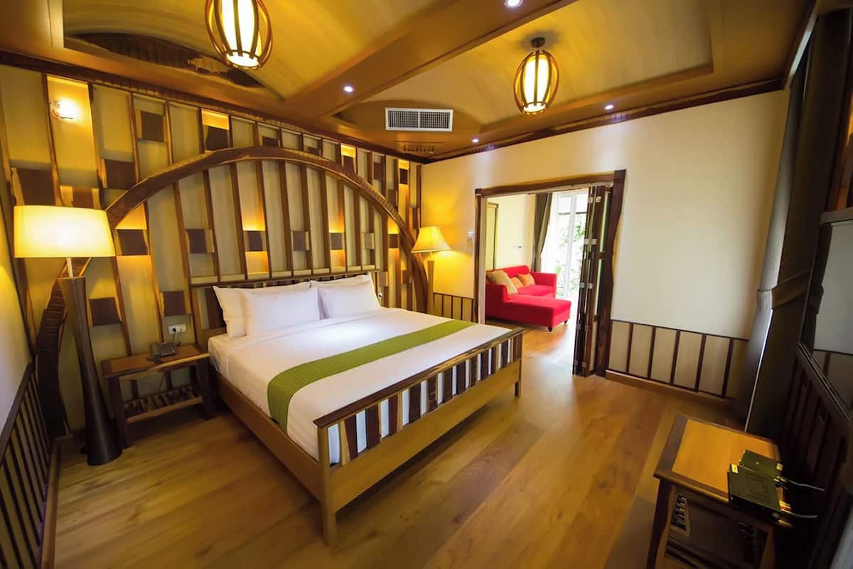 Una habitación de hotel con una cama de madera, una silla roja, un escritorio y un espejo grande.