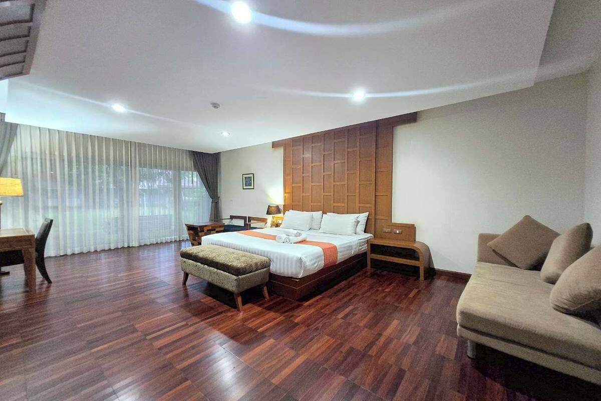 A modern hotel room with a large bed, a sofa, a desk, and a chair.