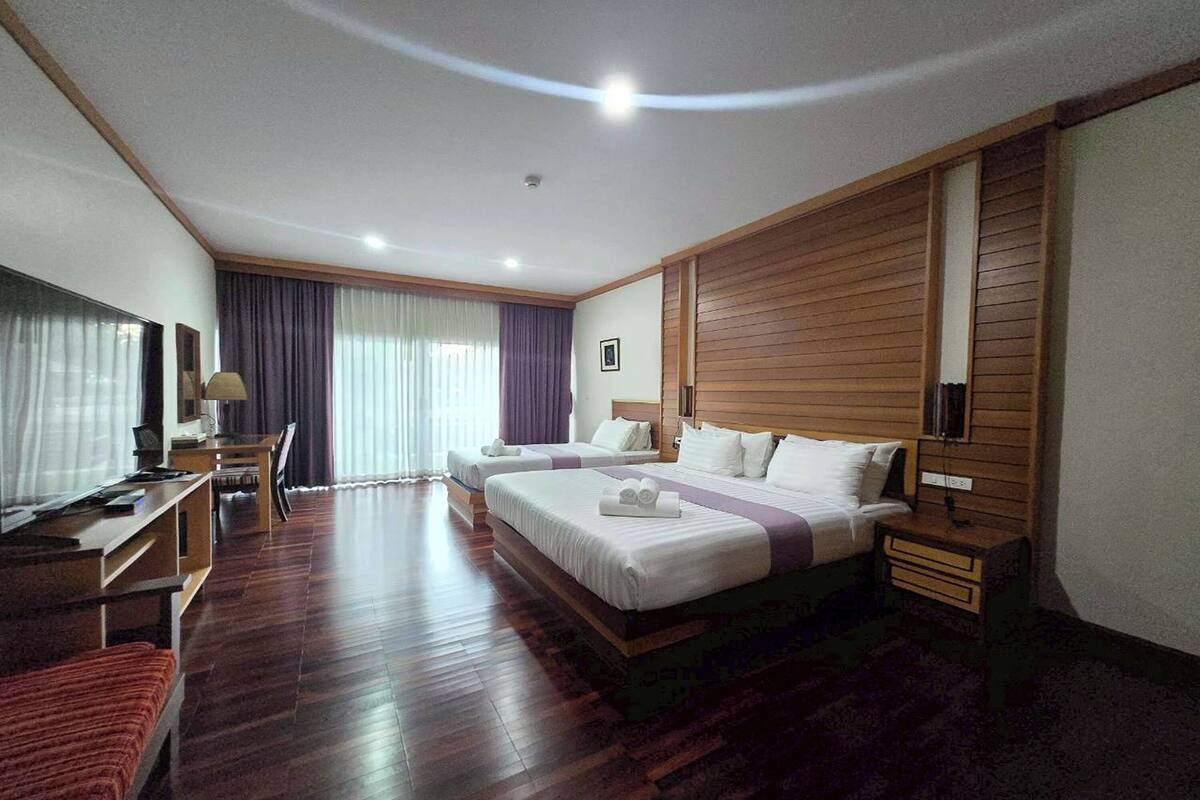 A hotel room with two beds, a desk, a TV, and a large window with curtains.