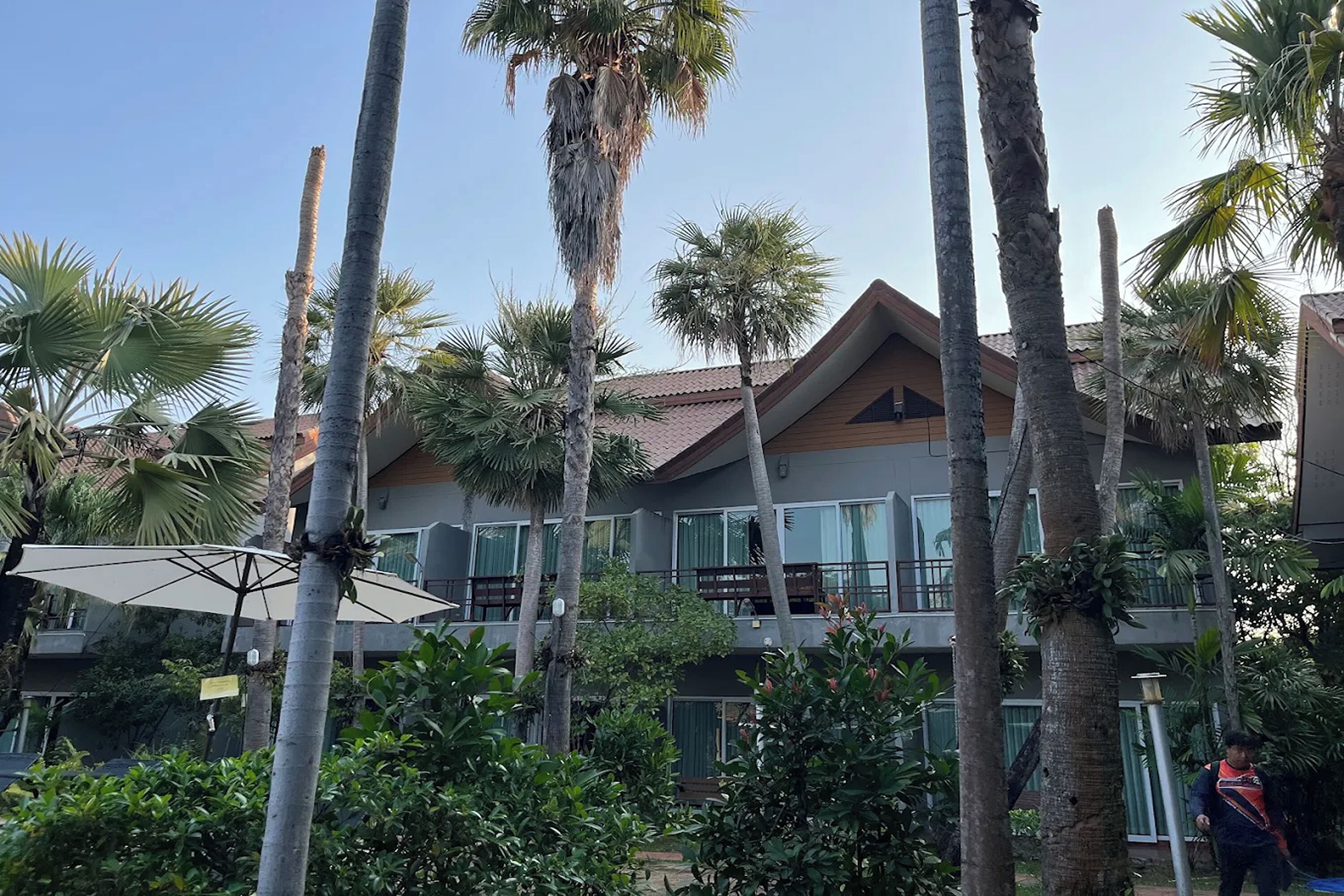 A multi-story building with balconies, surrounded by palm trees and other greenery.