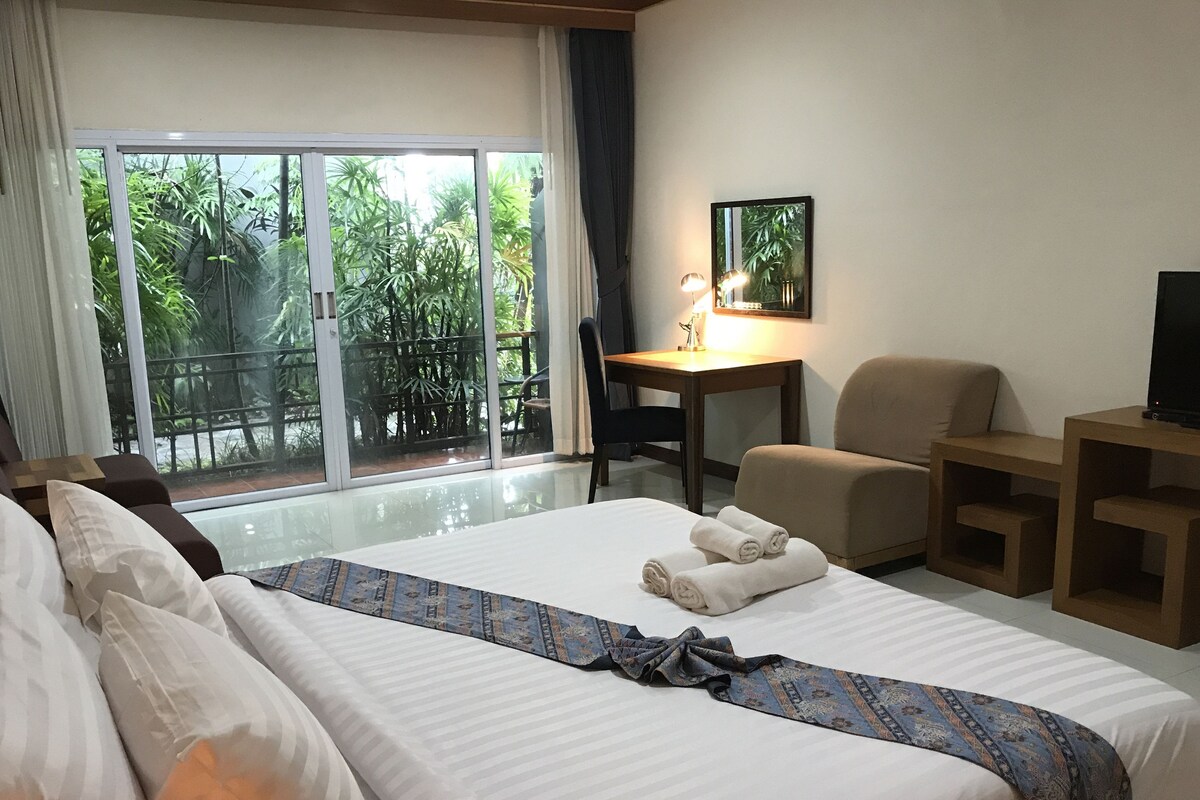 Une chambre d’hôtel équipée d’un lit, d’un bureau, d’une chaise, d’une télévision et d’un balcon agrémenté de plantes.