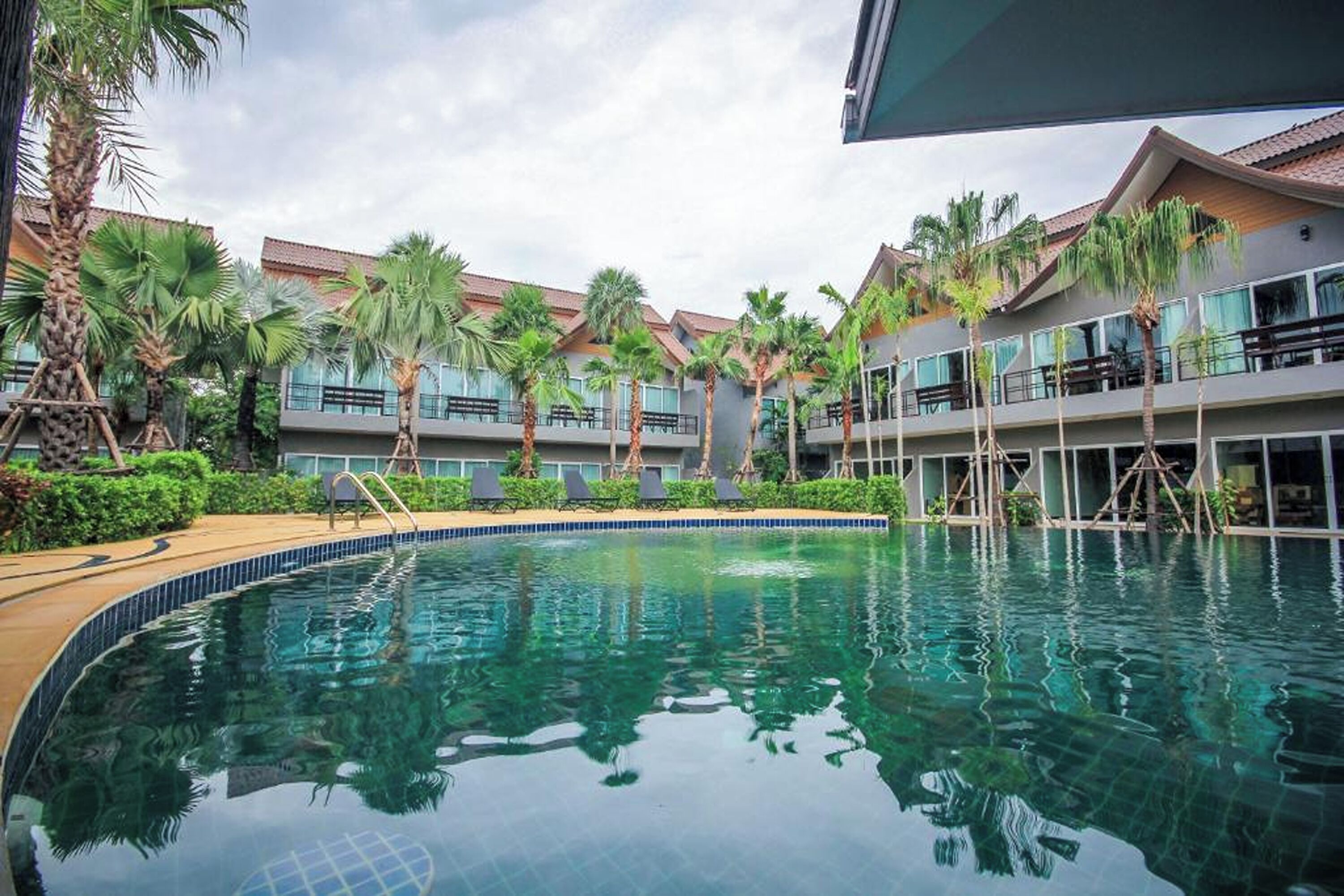 A swimming pool surrounded by palm trees and a building with balconies.