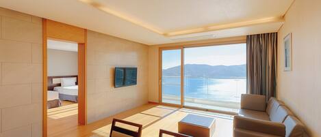 Una habitación de hotel moderna con un gran ventanal, un sofá, un televisor y un comedor.