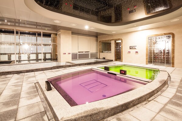 A modern indoor pool area with a purple and green pool, surrounded by stone walls and a glass enclosure. - Sono Calm Geoje (Geoje)