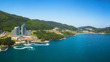 Vista aérea de una ciudad costera con modernos edificios de gran altura, un puerto deportivo con barcos y colinas verdes exuberantes al fondo.