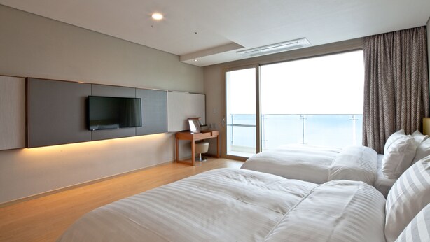Une chambre d’hôtel moderne dotée d’un grand lit, d’un bureau avec un téléviseur à écran plat et d’un balcon offrant une vue sur la mer.