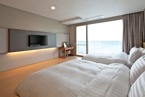 A modern hotel room with a large bed, a desk with a flat-screen TV, and a balcony with a view of the sea. - Sono Calm Geoje (Geoje)