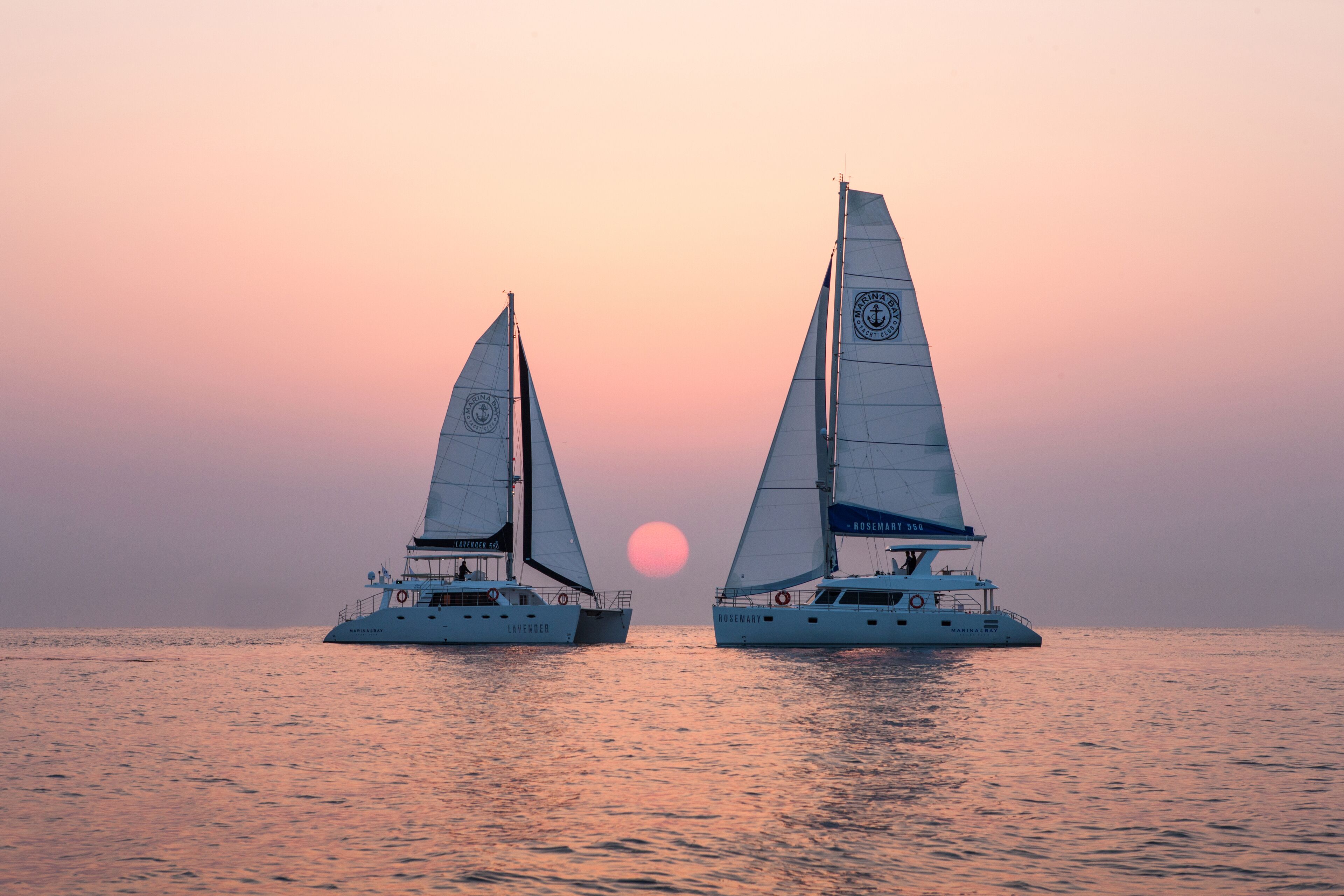 Two sailboats on calm waters with a sunset in the background.