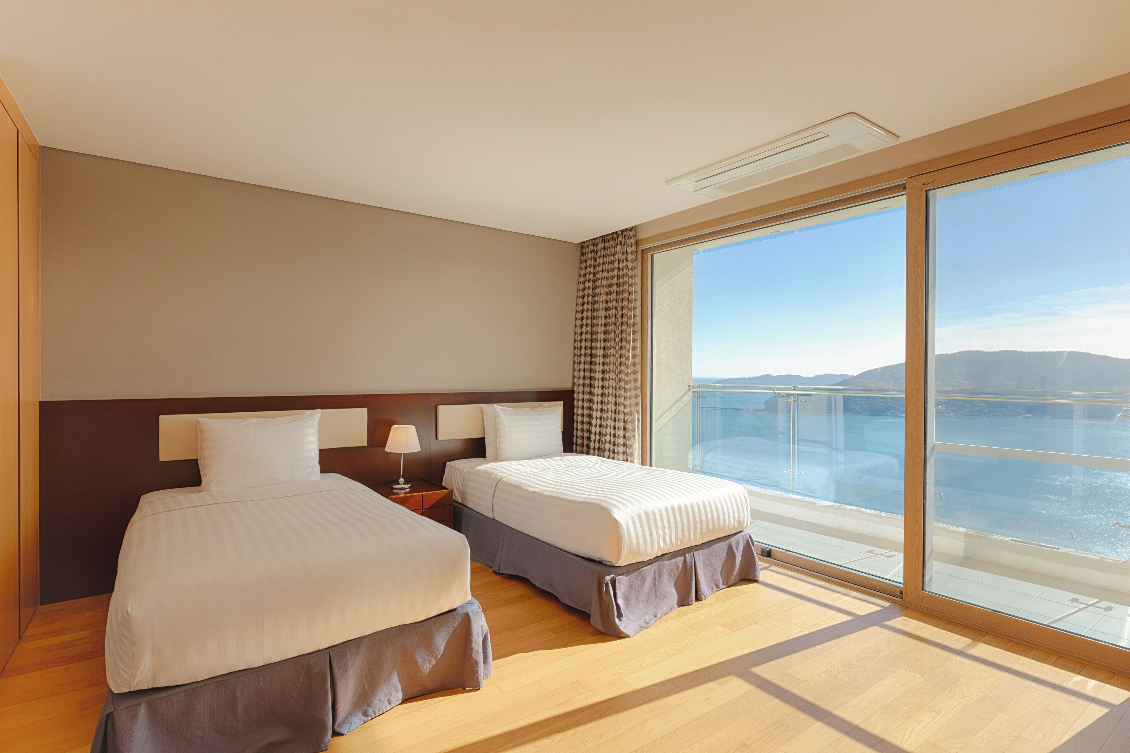 A hotel room with two beds, a large window with a view of the sea, and a modern design.