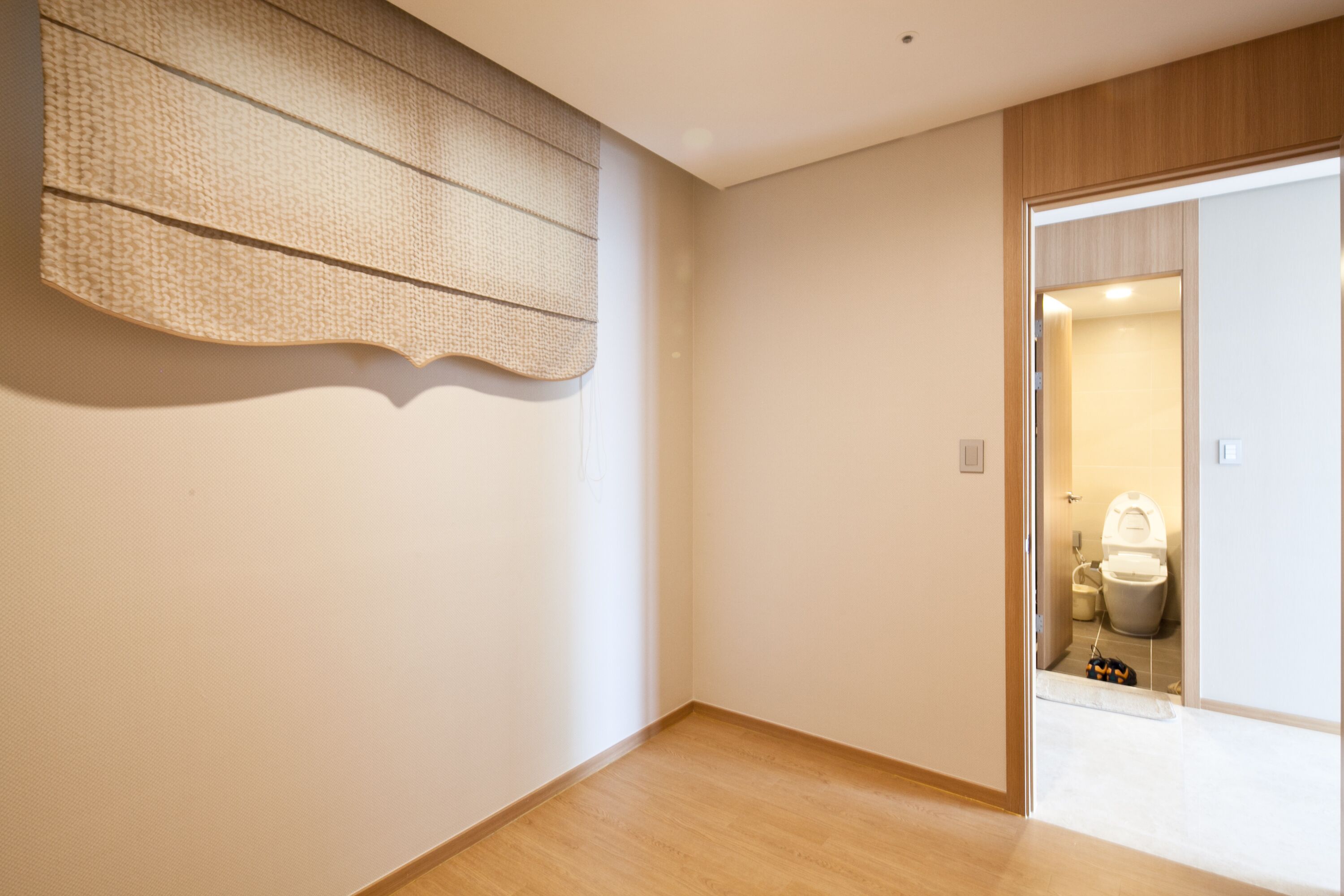 A room with a wooden floor, a large woven wall hanging, and a doorway leading to a bathroom with a toilet and a sink.