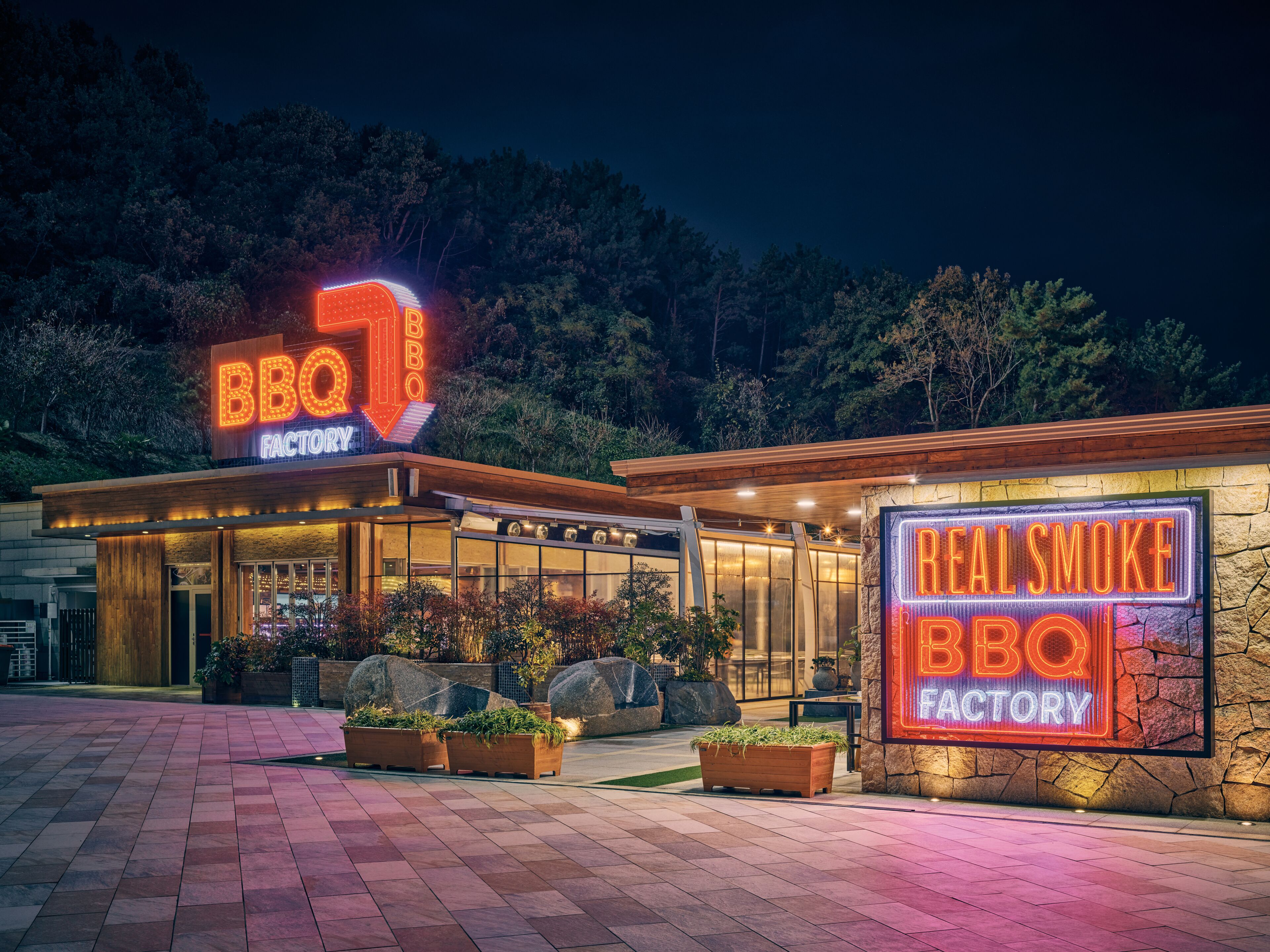 A BBQ factory with a neon sign, outdoor seating, and a stone facade.