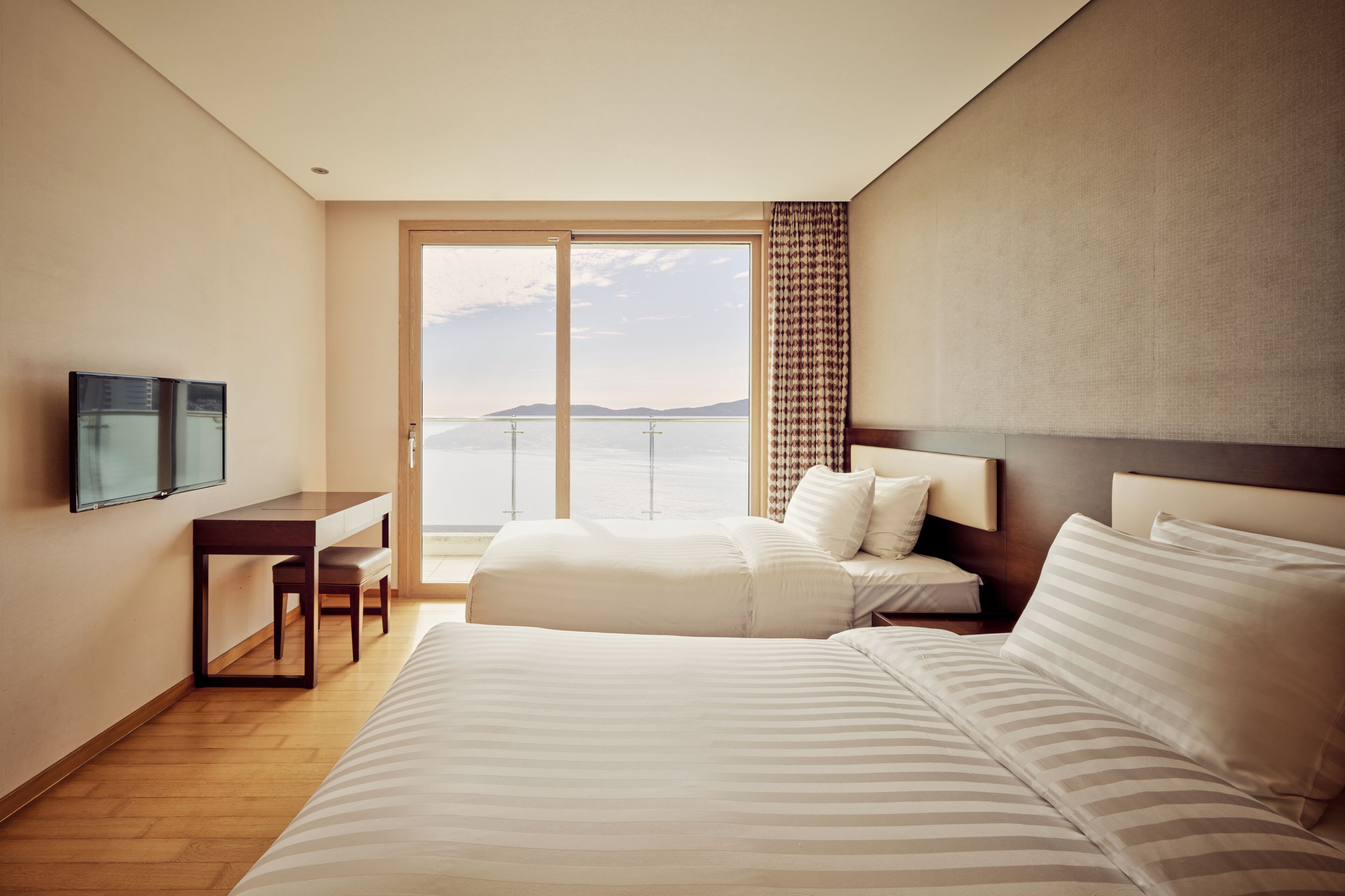 A hotel room with a large bed, a desk with a chair, a TV, and a view of the sea.