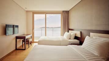 A hotel room with a large bed, a desk with a chair, a TV, and a view of the sea.