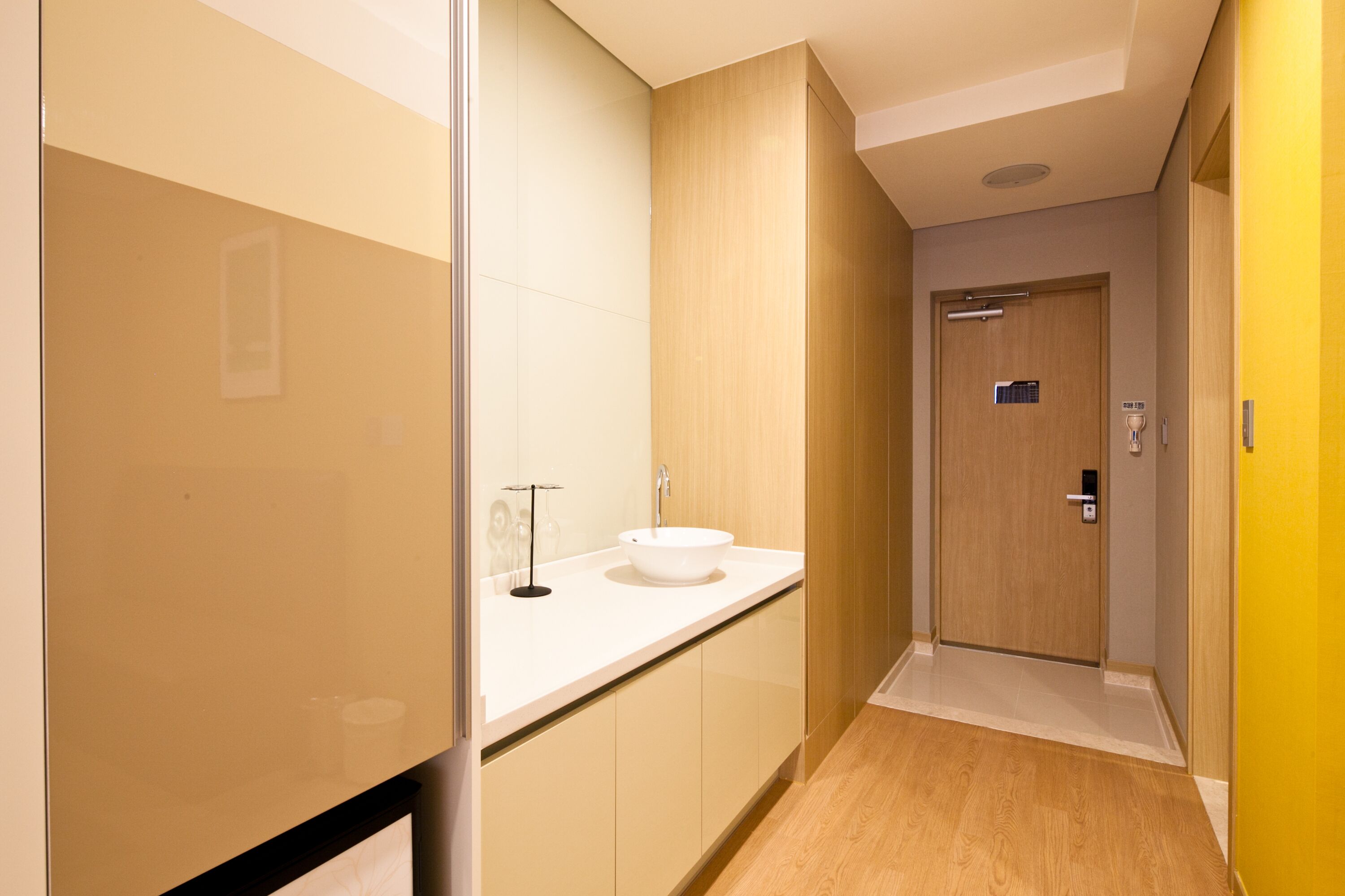 A modern bathroom with a white sink, wooden cabinets, and a wooden door.