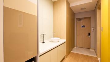 A modern bathroom with a white sink, wooden cabinets, and a wooden door.