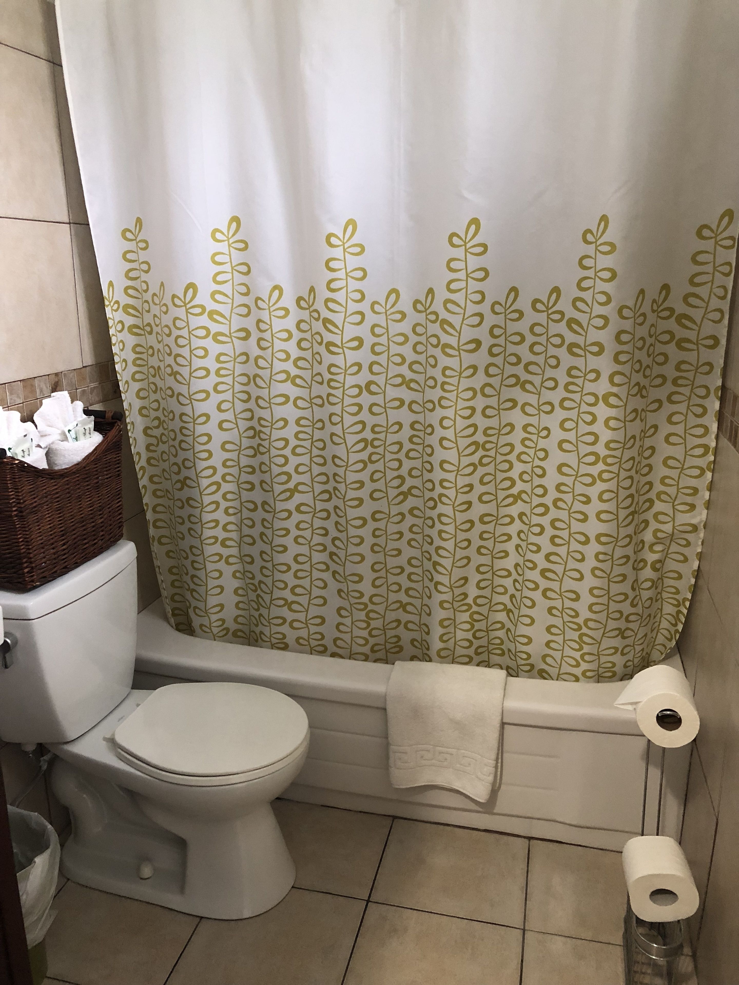 Un baño con inodoro, bañera y cortina de ducha estampada, además de una cesta de toallas.