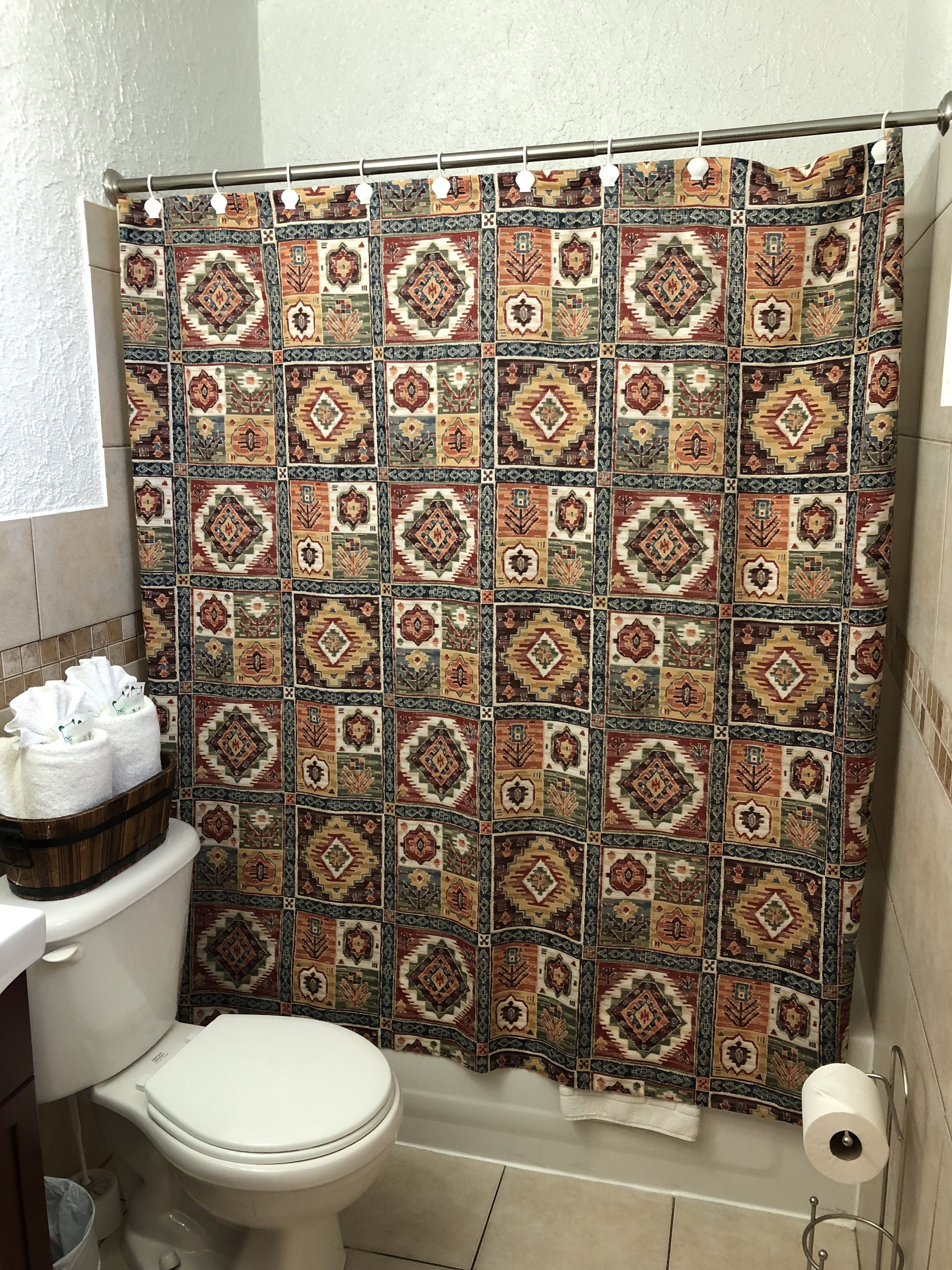 A bathroom with a patterned shower curtain, a toilet, a towel rack with towels, and a toilet paper holder.
