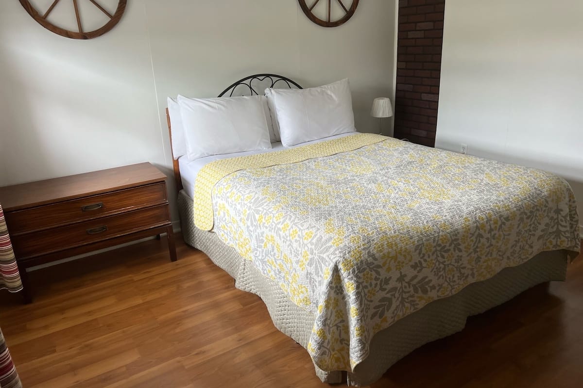 A neatly made bed with a patterned bedspread, a wooden nightstand with drawers, and two wall-mounted wooden wheels.