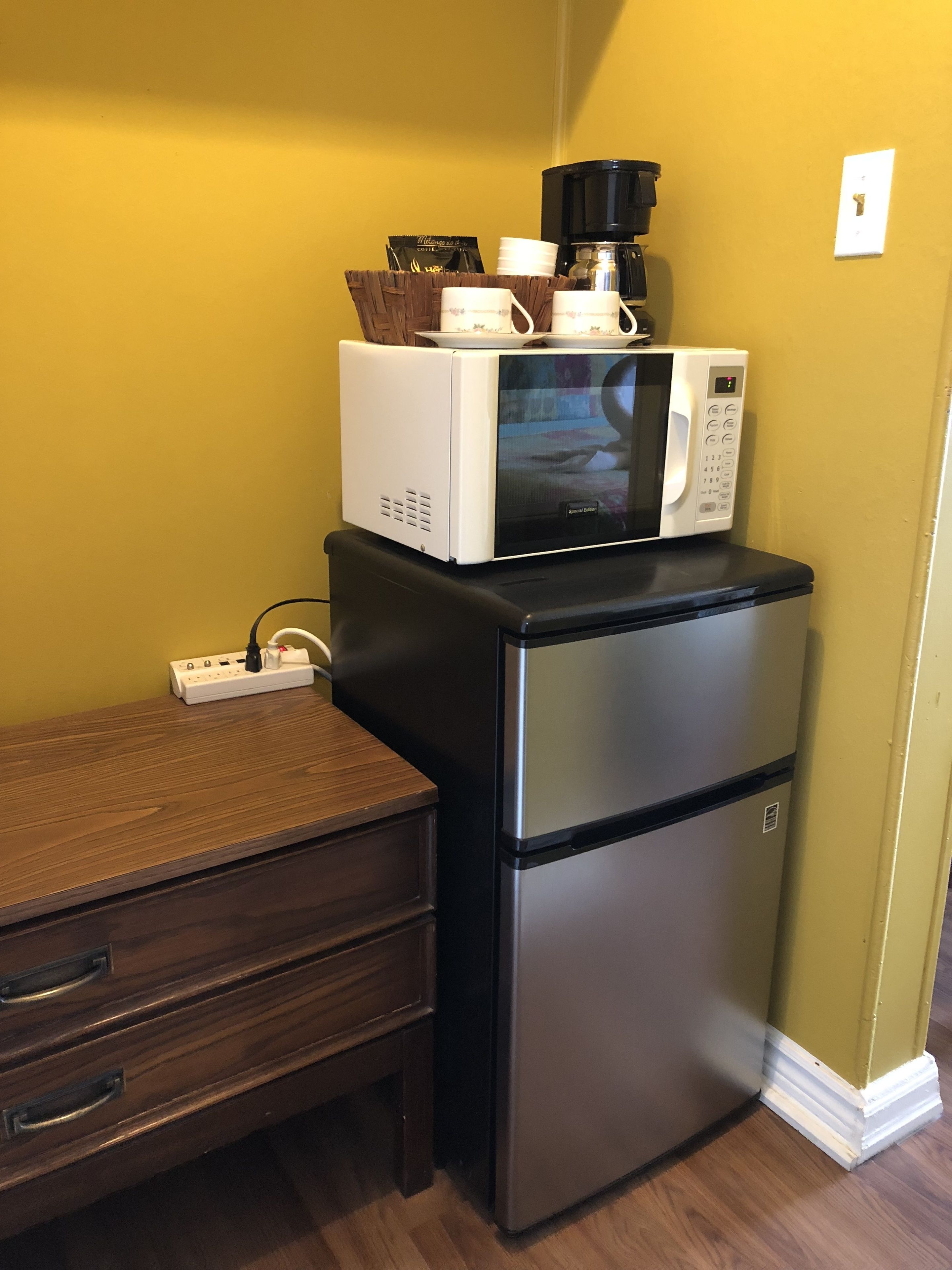 A compact kitchen with a refrigerator and a microwave on top, a wooden countertop, and a power strip.