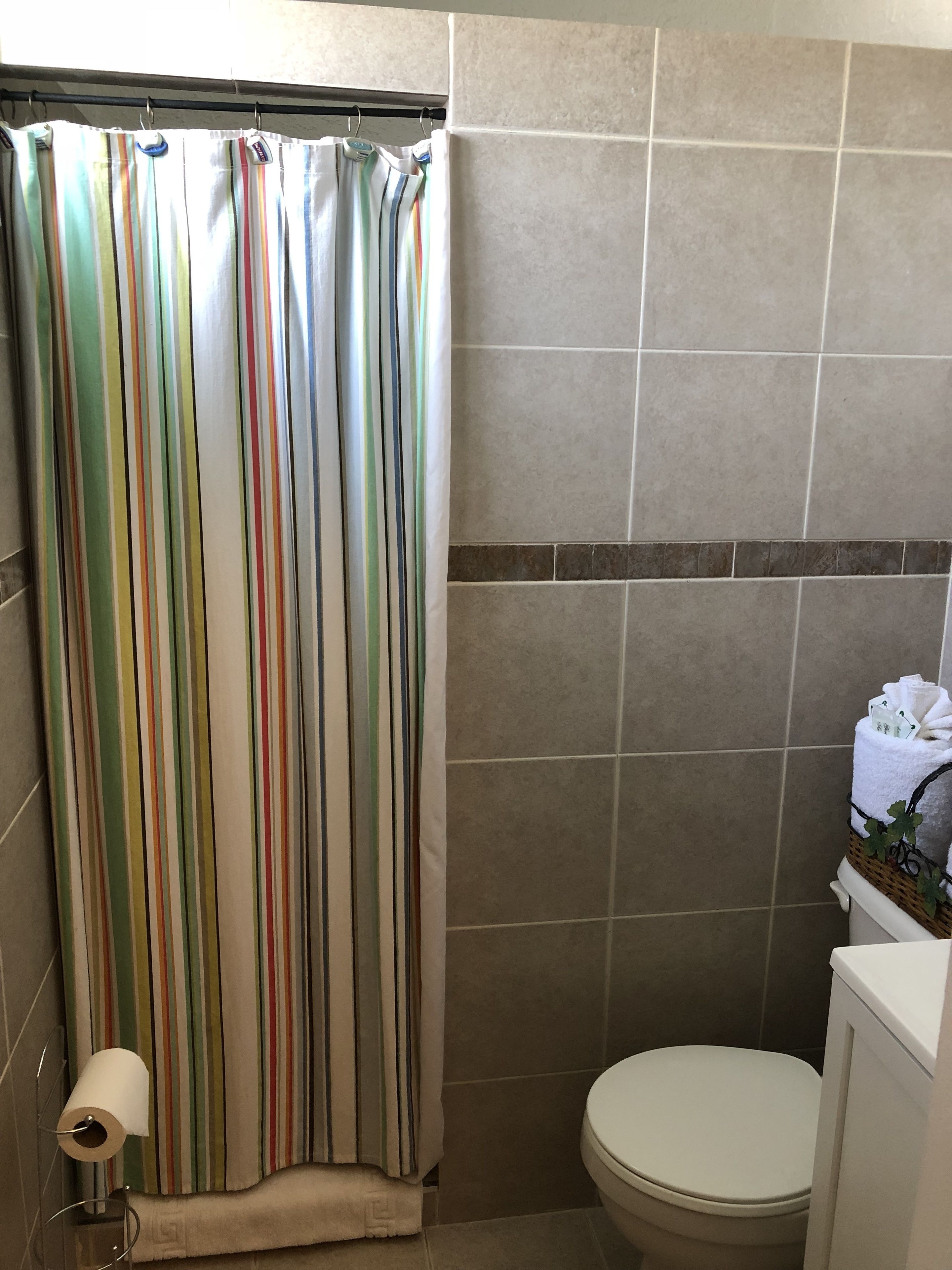 Un baño con cortina de ducha a rayas, un inodoro y una pequeña cesta de mimbre con artículos de aseo.