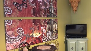A room with a green wall, a flat-screen TV, a decorative hanging lantern, a two-tiered metal table with chairs, and two large paintings with floral and butterfly motifs. - The Rex Motel (Niagara Falls)