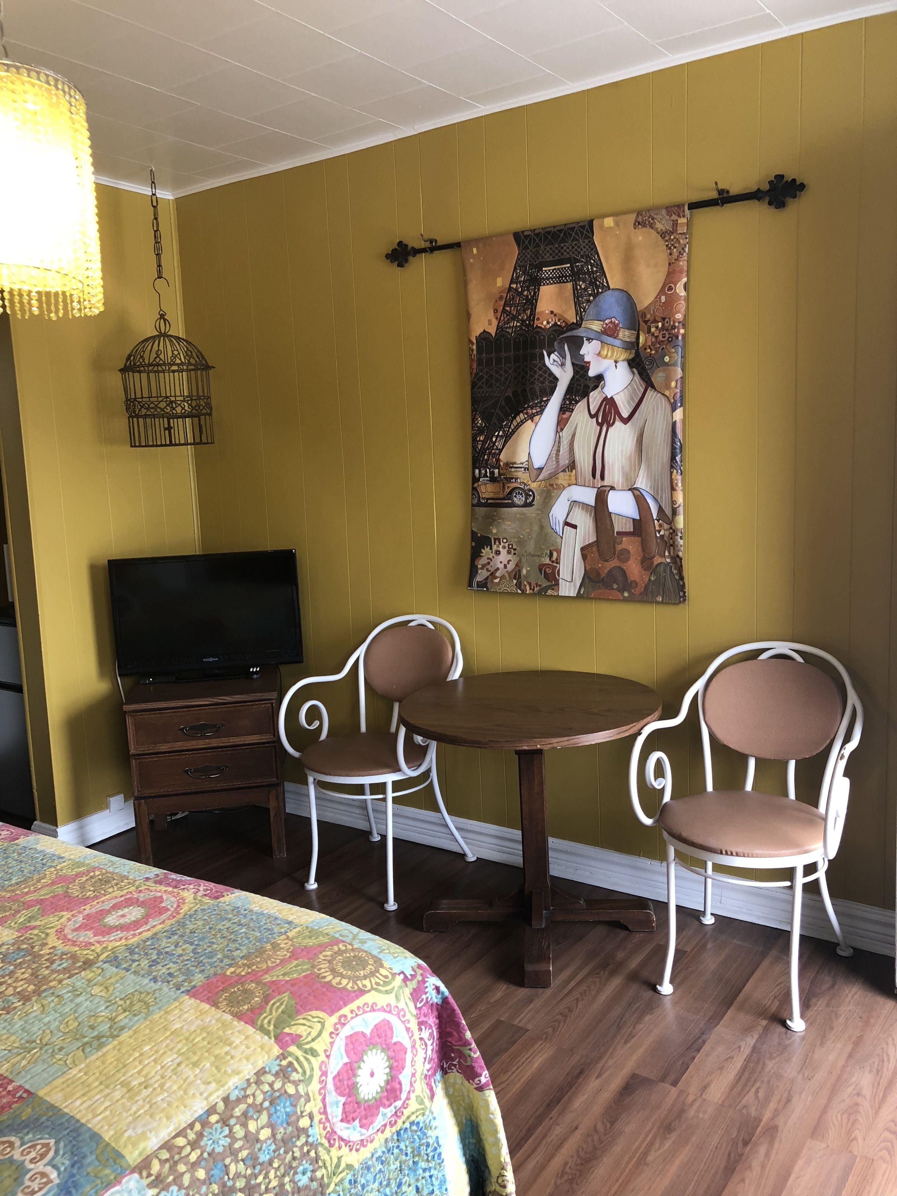 Une chambre avec un lit, une télévision, une table, deux chaises et un tableau représentant une femme devant la Tour Eiffel.
