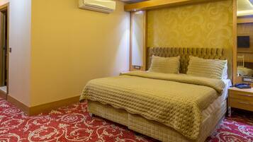 A hotel room with a large bed, a bedside table, an air conditioner, and a patterned carpet.