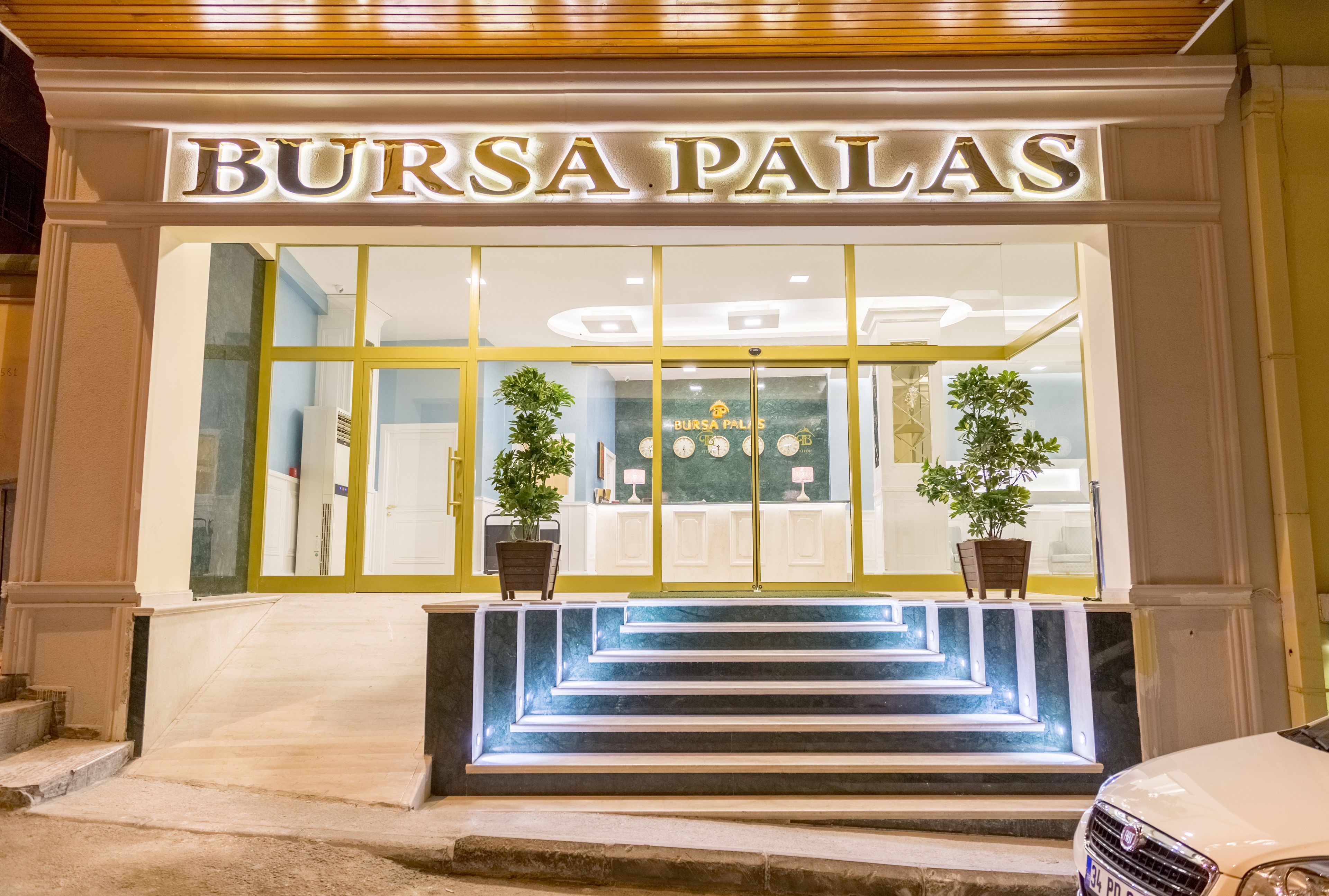 The entrance to Bursa Palas with a clear sign, steps leading up to the entrance, and two potted plants on either side.