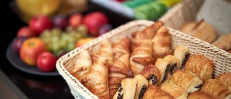 A basket of croissants and a plate of apples and grapes.