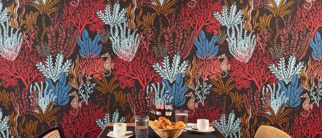 A dining area with a table set for two, chairs, and a patterned wallpaper.
