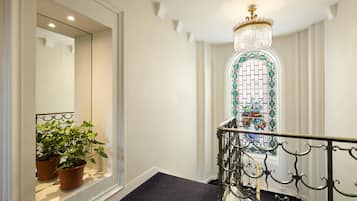 A staircase with a black metal railing, a chandelier, and a stained glass window.