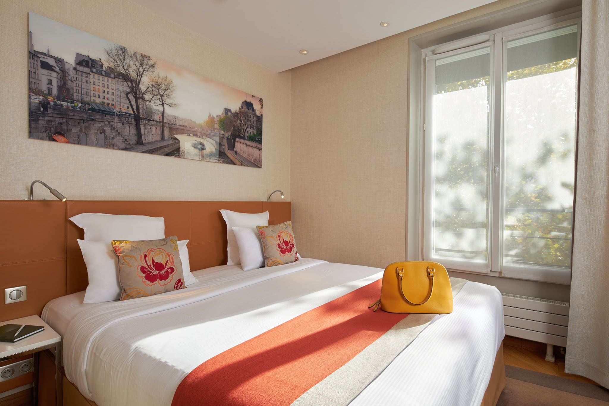 A hotel room with a bed, a nightstand, a window with curtains, and a painting on the wall.
