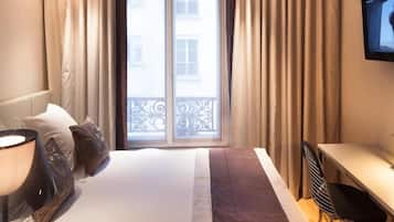 A hotel room with a bed, a desk, a chair, a television, and a window with curtains.