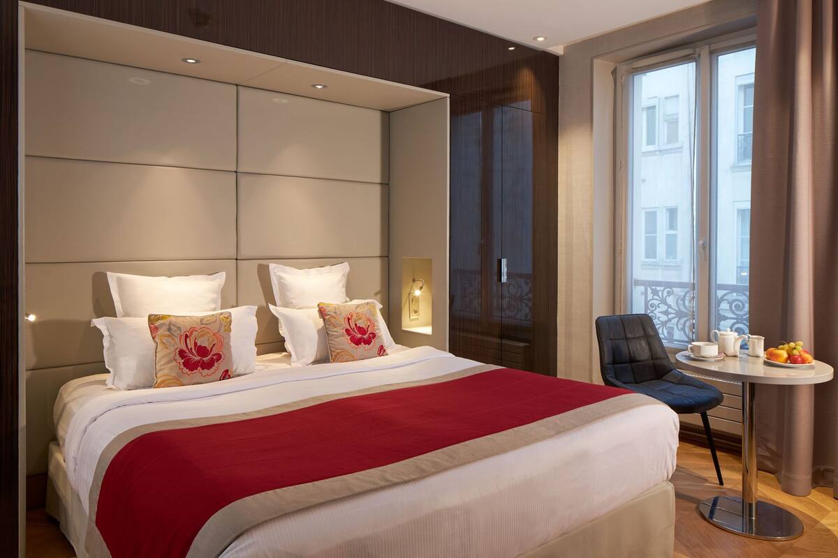 A hotel room with a large bed, a small table with a cup and fruit, and a chair.